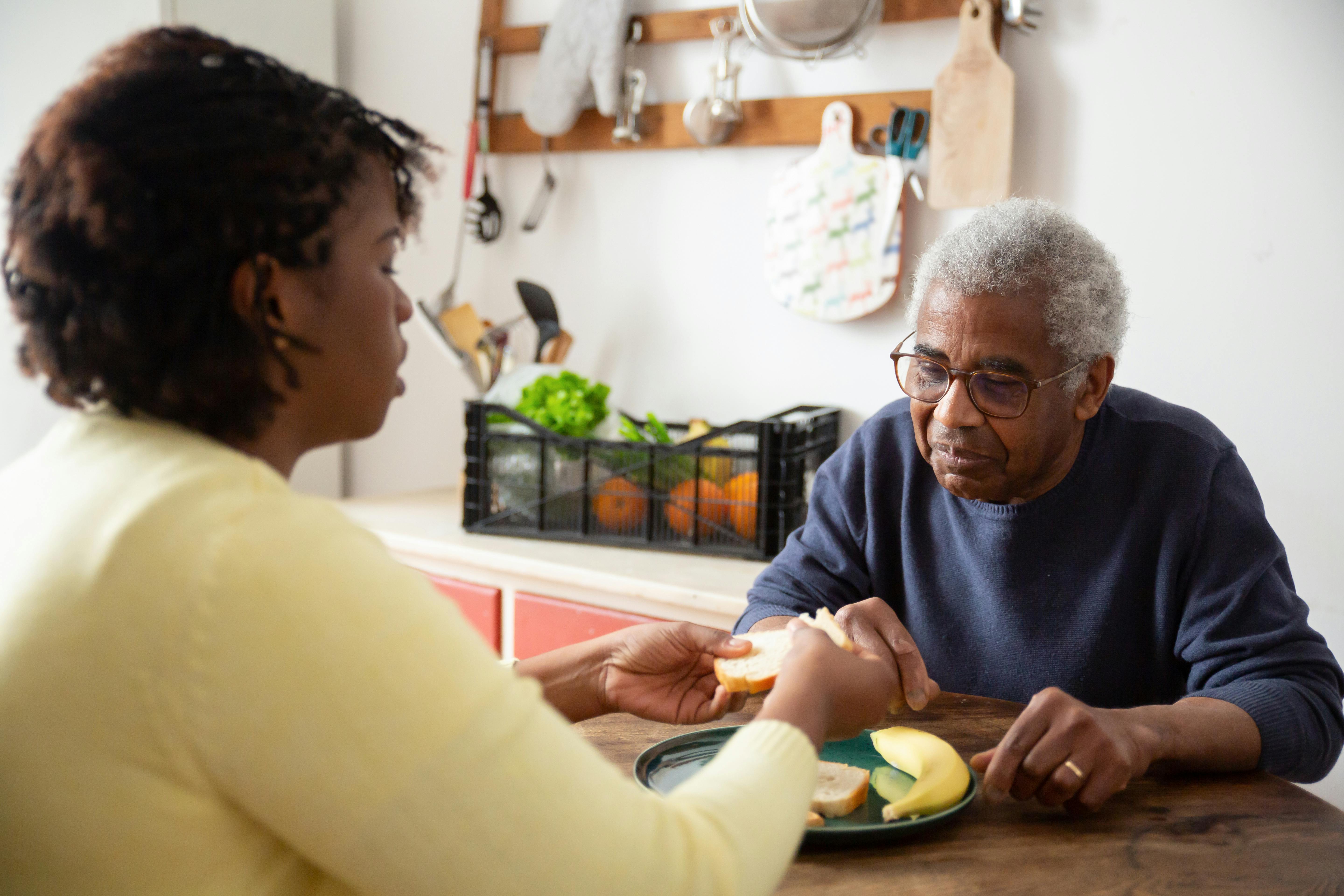 Caregiver helping elderly man with a meal at the table