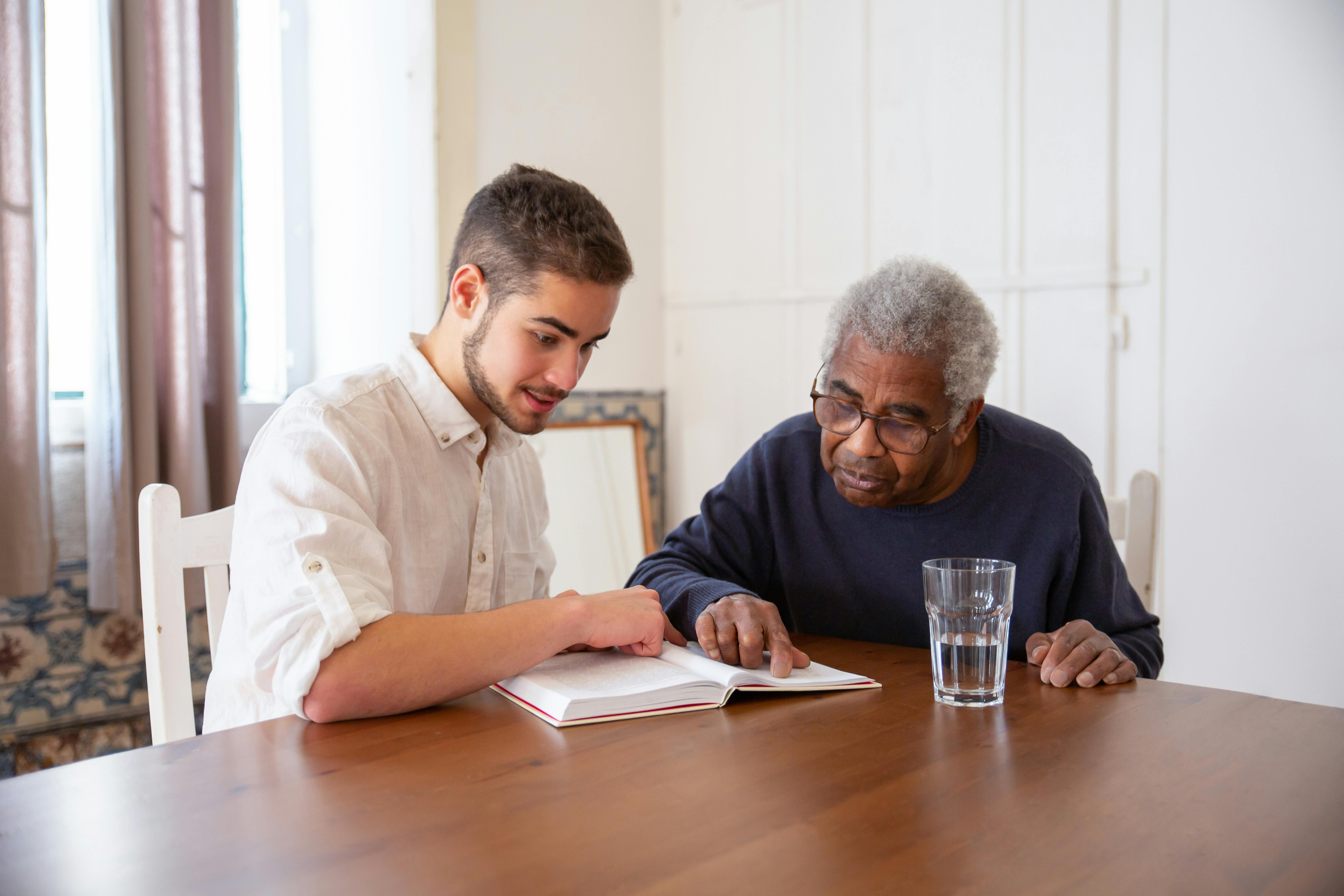 Young man reading a book with elderly man at a table